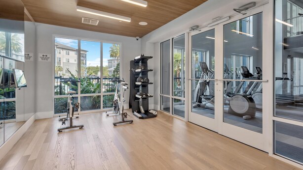 Ein Fitnessraum mit Trainingsgeräten, großen Fenstern und einer Holzbalkendecke.