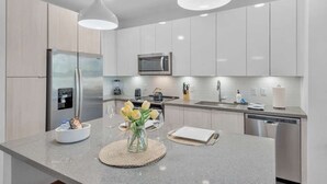 Eine moderne Küche mit Edelstahlgeräten, einer zentralen Kochinsel, Pendelleuchten und einem klaren, minimalistischen Design.