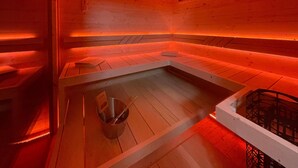 Ein Saunaraum mit Holzwänden und -bänken, einem Metallbecken und einer Holzbank mit Handtuch.