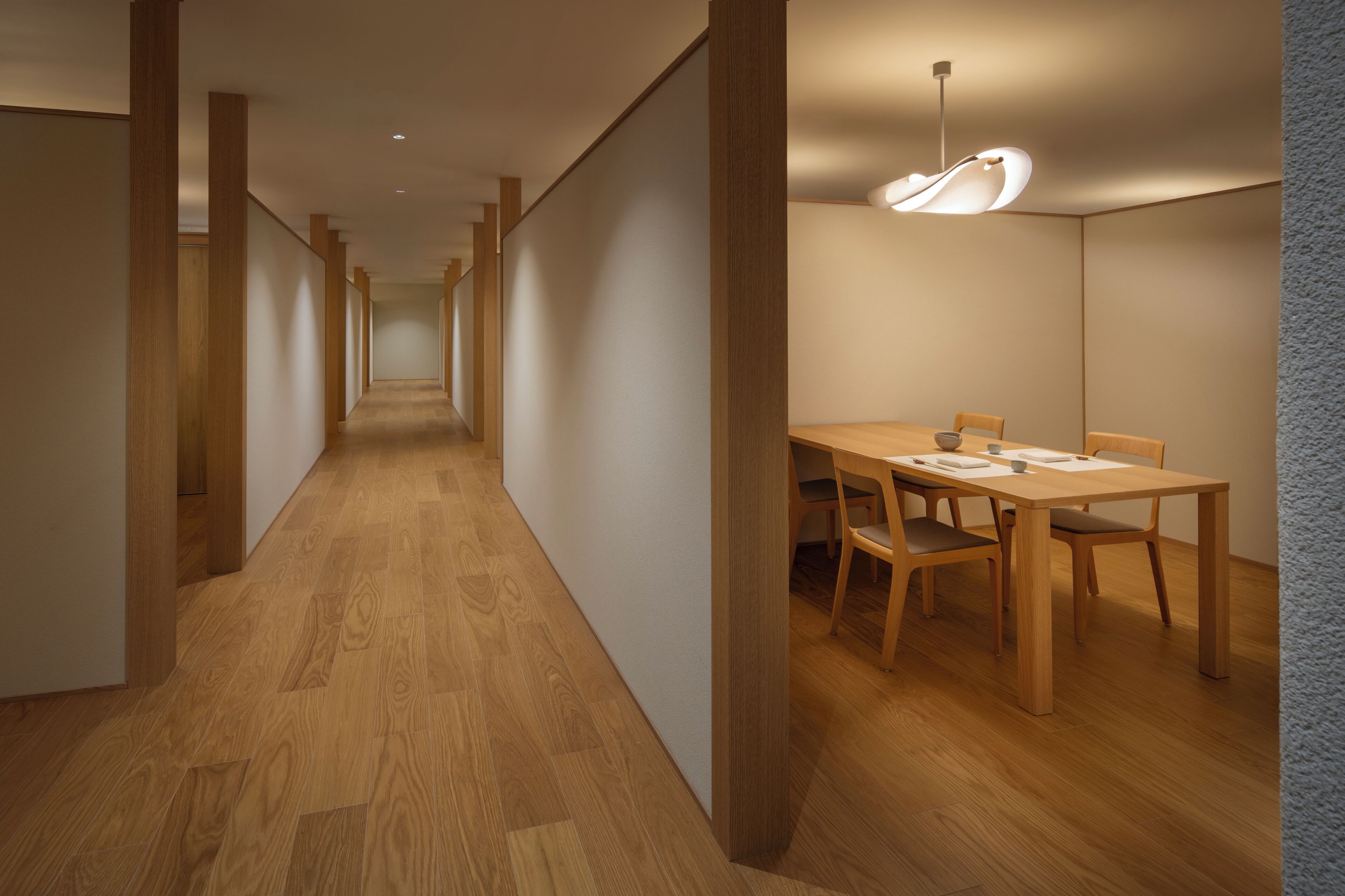 Un pasillo con piso y paredes de madera que conduce a un comedor con mesa y sillas.