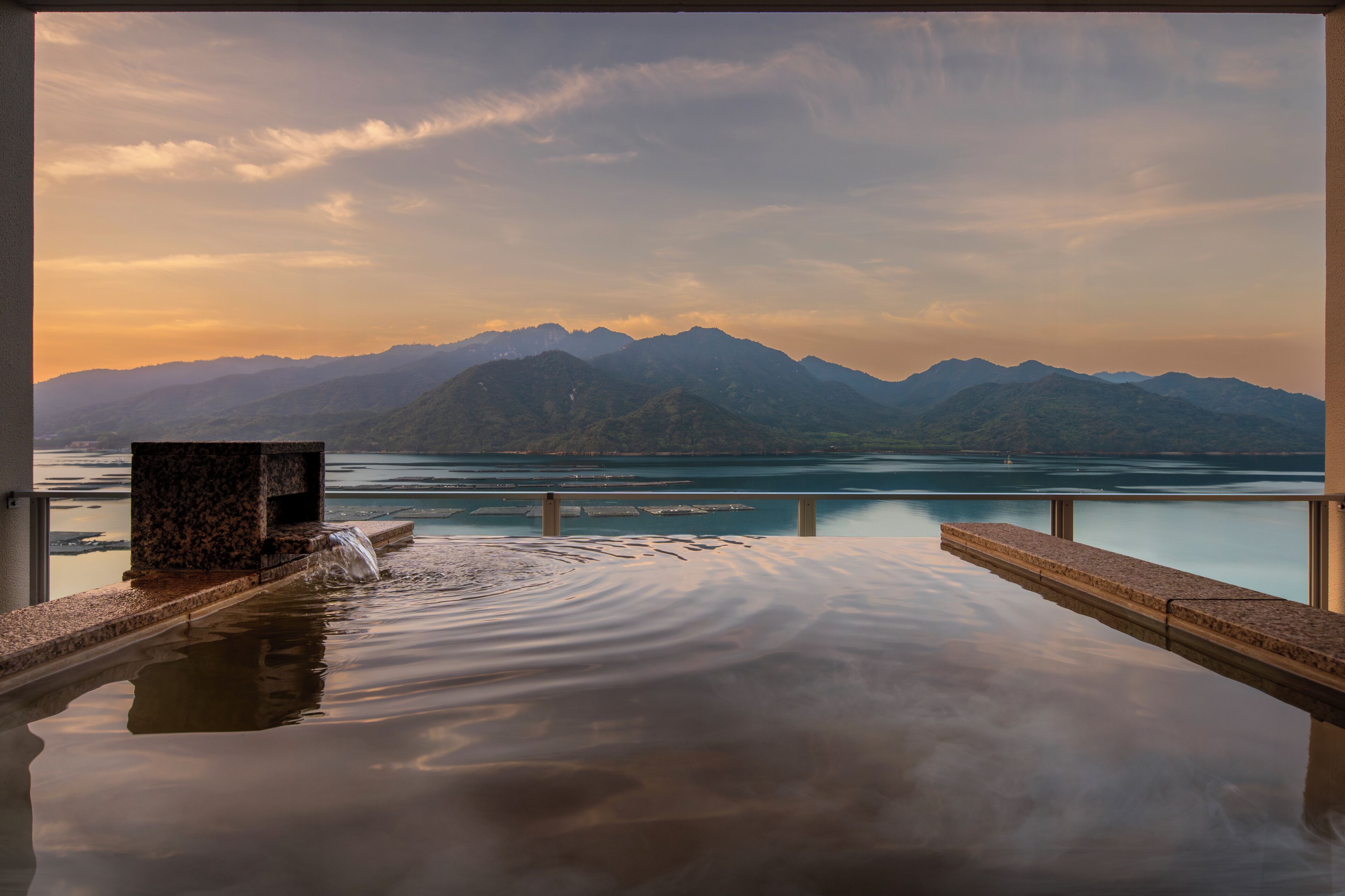 Una tranquila piscina infinita con vistas a montañas y a un lago.