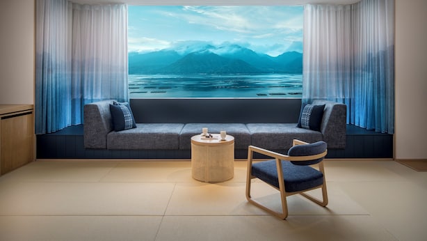 A room with a sofa, a round table, and a chair, with a view of mountains and water through a large window. - Hoshino Resorts KAI Miyajima (Hatsukaichi)