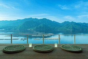 A deck with three green circular cushions, a glass of water, and a view of a calm lake with mountains in the background. - Hoshino Resorts KAI Miyajima (Hatsukaichi)