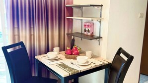 Un comedor con una mesa preparada para dos, una silla, un estante con objetos y una cortina.