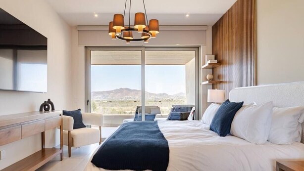 Quarto com cama grande, escrivaninha, cadeira, televisão e vista para o exterior.