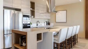 Cozinha moderna com ilha central, eletrodomésticos de aço inoxidável e área de bar com banquetas.
