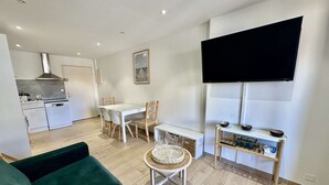 A compact living space with a kitchenette, a dining area, a sofa, a TV, and a small table with a basket. - IN THE HEART OF THE CITY CENTER, ONE BEDROOM APARTMENT FOR 4 PEOPLE (STE MAXIME)