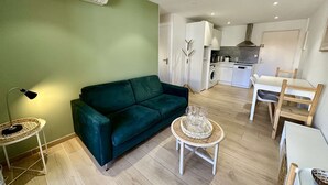 A compact living space with a green wall, a sofa, a dining table with chairs, a small round table with a tray, and a kitchen area with a washing machine and a stove. - IN THE HEART OF THE CITY CENTER, ONE BEDROOM APARTMENT FOR 4 PEOPLE (STE MAXIME)