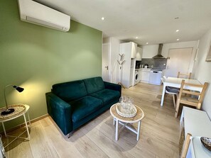 A compact living space with a green wall, a sofa, a dining table with chairs, a small round table with a tray, and a kitchen area with a washing machine and a stove. - IN THE HEART OF THE CITY CENTER, ONE BEDROOM APARTMENT FOR 4 PEOPLE (STE MAXIME)
