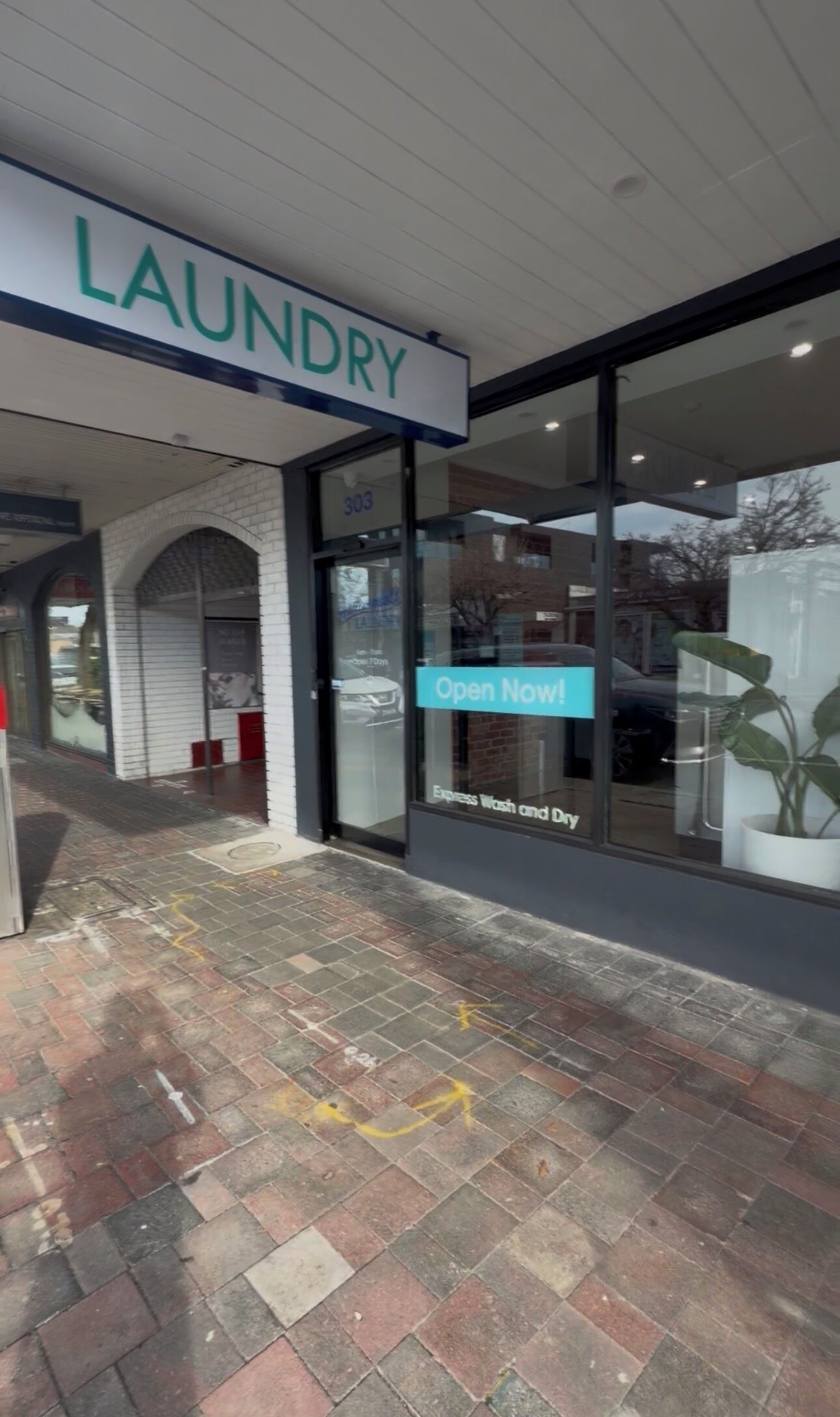 Une devanture de magasin avec une enseigne indiquant « LAUNDRY » et une vitrine faisant la publicité de l’ouverture immédiate, avec un message sur les services de lavage et de séchage rapides.