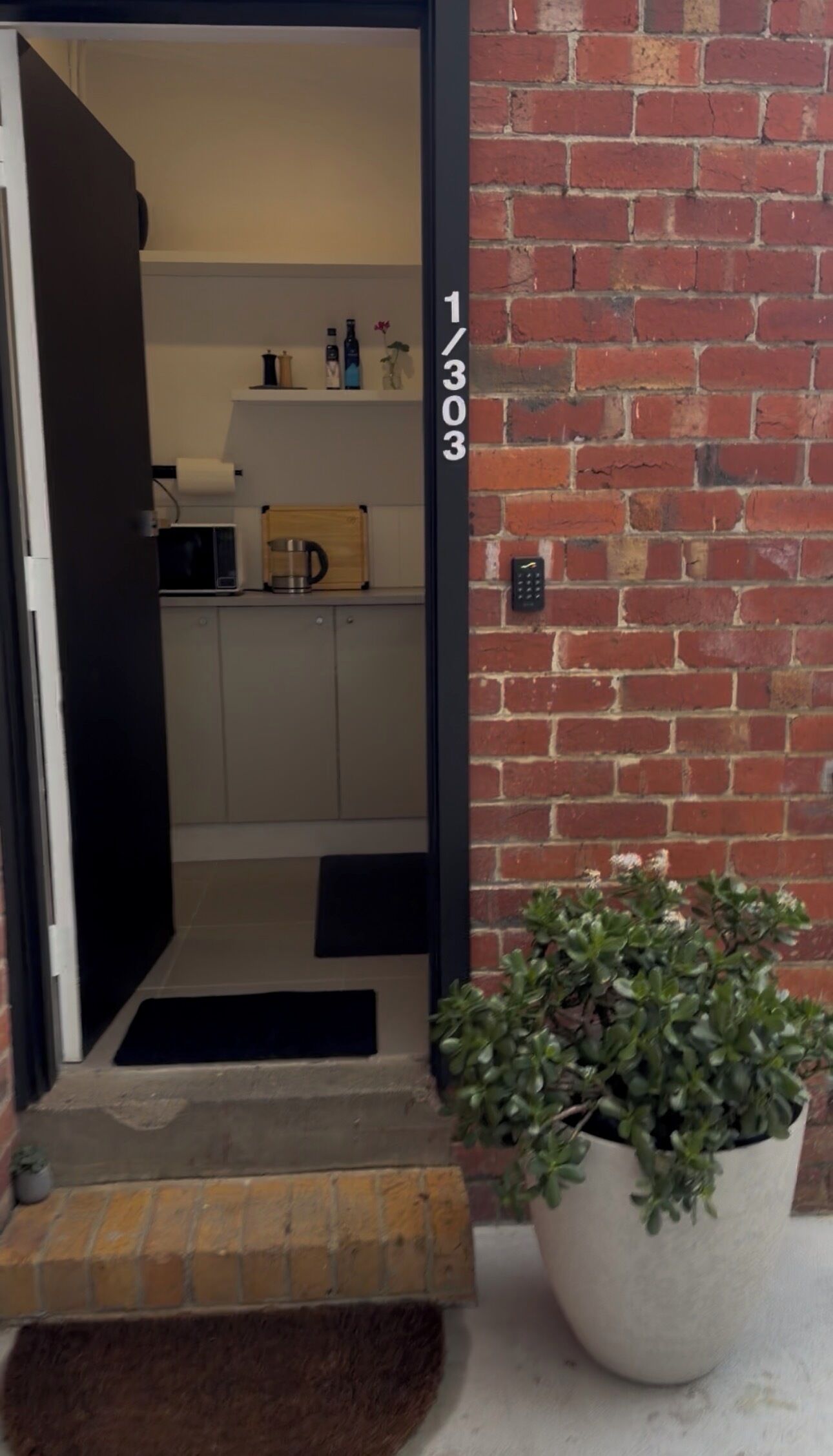 A doorway leading to a kitchen with a microwave, a coffee maker, and a shelf with bottles.