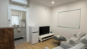 A modern living room with a grey sofa, a flat-screen TV, and a white entertainment unit. - Everything at your doorstep. 25-minute train ride to the heart of the city. (Oakleigh)
