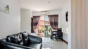 Ein modernes Wohnzimmer mit Ledersofa, Essbereich mit Tisch und Stühlen sowie eine Glastür, die zu einem Außenbereich führt.