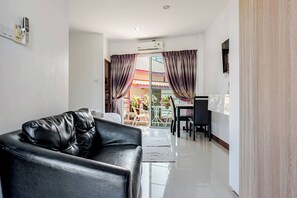 A modern living room with a leather sofa, a dining area with a table and chairs, and a sliding glass door leading to an outdoor space. - VK Living Room 20 min Walk to Kata Beach #302 (Karon)