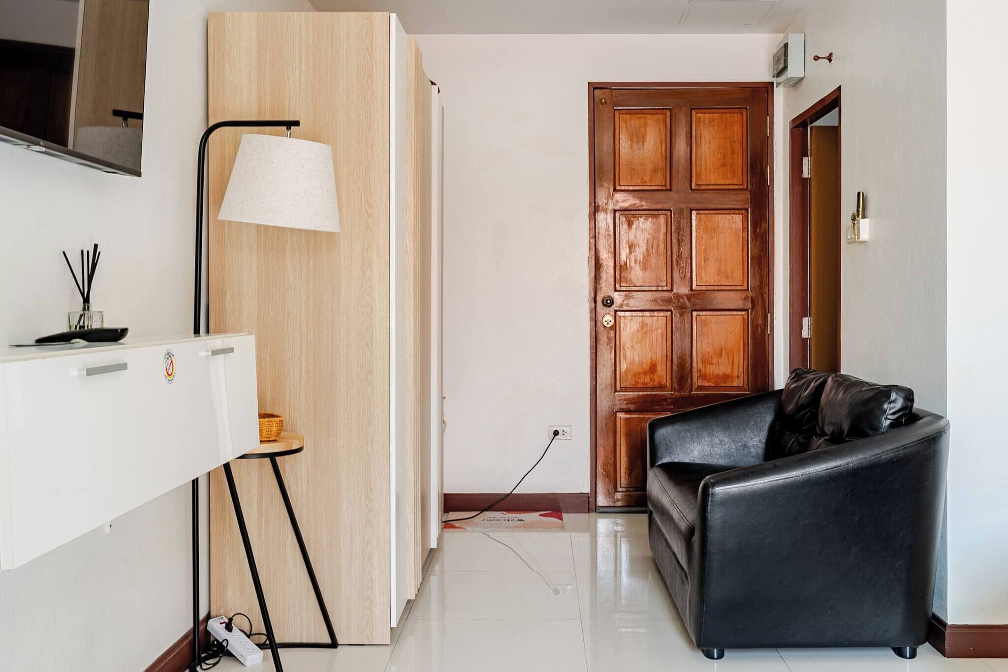 Un saló modern amb un sofà de cuir negre, una porta de fusta i un moble blanc amb una làmpada.