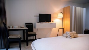 Ein Hotelzimmer mit einem Bett, einem Schreibtisch mit Fernseher, einem Sessel und einer Lampe.