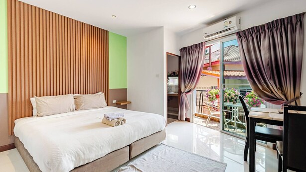 Ein Schlafzimmer mit Bett, Schreibtisch und einem Balkon mit Blumen.