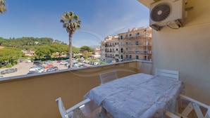Un balcon avec une table et des chaises, un palmier, et une vue sur un parking et des immeubles.