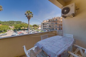 A balcony with a table and chairs, a palm tree, and a view of a parking lot and buildings. - APPARTAMENTI GLI ORIZZONTI - ORIZZONTI BILO 17 (Marina di Campo)