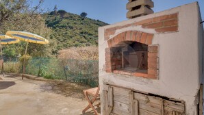 A brick-built outdoor oven with a chimney, a wooden bench, and a green fence in the background. - Sunset Goelba - where the rock meets the sea (Marciana)