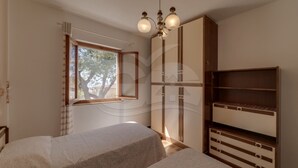 A bedroom with two beds, a wardrobe, and a window with a view of trees. - Sunset Goelba - where the rock meets the sea (Marciana)