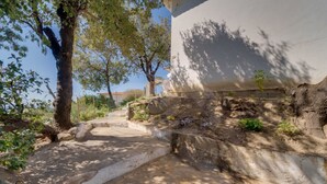 A stone pathway leading to a building with a white wall and a tree-lined path. - Sunset Goelba - where the rock meets the sea (Marciana)
