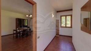 A spacious hallway with a dining area, a window with a view of greenery, and a wooden door. - Sunset Goelba - where the rock meets the sea (Marciana)