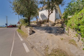 A rural road with a stone wall and a white building with a sloped roof.