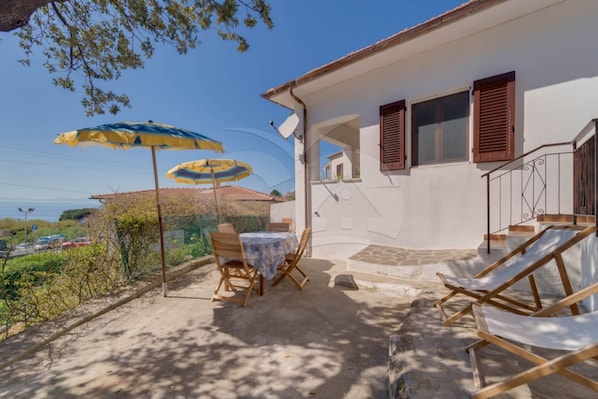 A patio with a table and chairs, a blue and yellow umbrella, and a view of the sea.