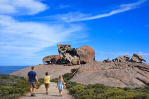 A family walking on a path towards a large rock formation with a clear sky above.