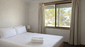 Une chambre d’hôtel avec un lit, une table de chevet, une lampe et une fenêtre avec des rideaux.