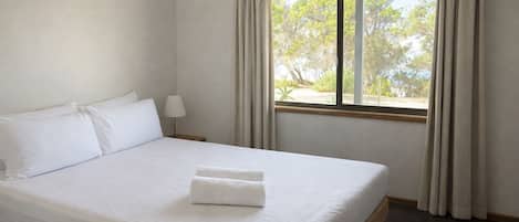 Una habitación de hotel con cama, mesita de noche, lámpara y ventana con cortinas.