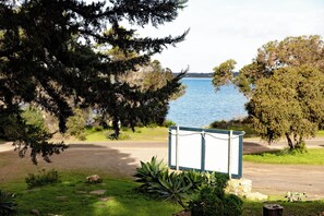 A coastal view with a signboard in the foreground, a road, and a body of water in the background.