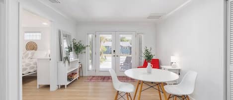 A modern, well-lit room with a round table, white chairs, a red chair, and a white cabinet with shelves.