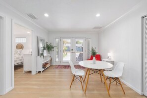 A modern, well-lit room with a round table, white chairs, a red chair, and a white cabinet with shelves. - Cozy Bungalow near Siesta Key Beach and Downtown (Sarasota)