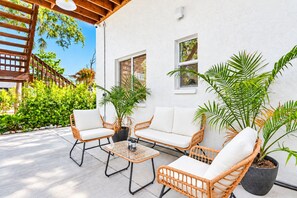 A patio with wicker furniture, potted plants, and a white wall. - Cozy Bungalow near Siesta Key Beach and Downtown (Sarasota)