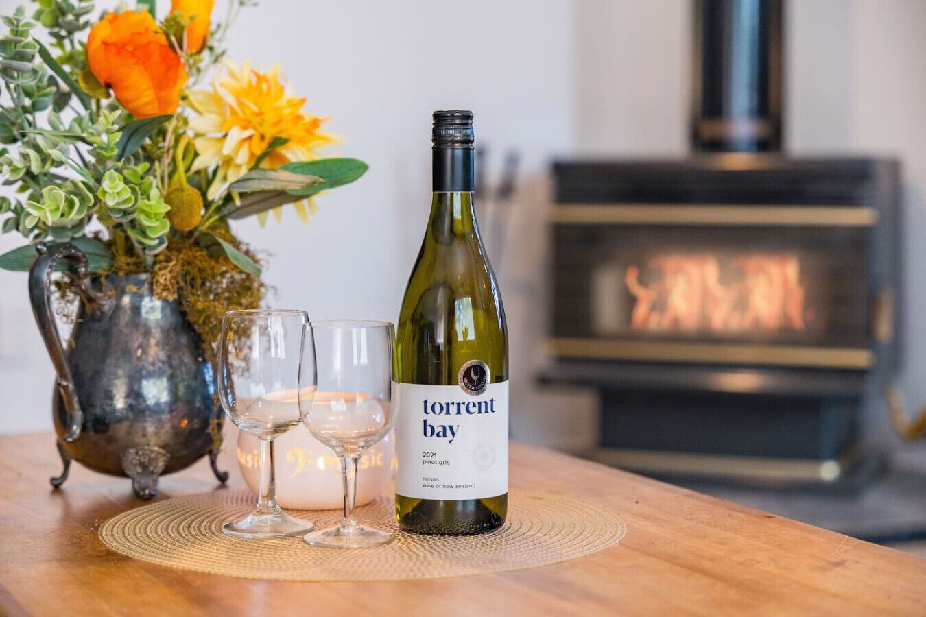 A bottle of wine, two glasses, and a vase with flowers on a wooden table.