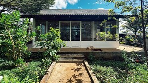 A modern house with a glass door, surrounded by lush greenery and a concrete pathway. - An Nhiên Farm dormitory with bunk beds (Pleiku)