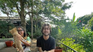 A wooden table with baskets of food, a dog, and a person holding a basket. - An Nhiên Farm dormitory with bunk beds (Pleiku)