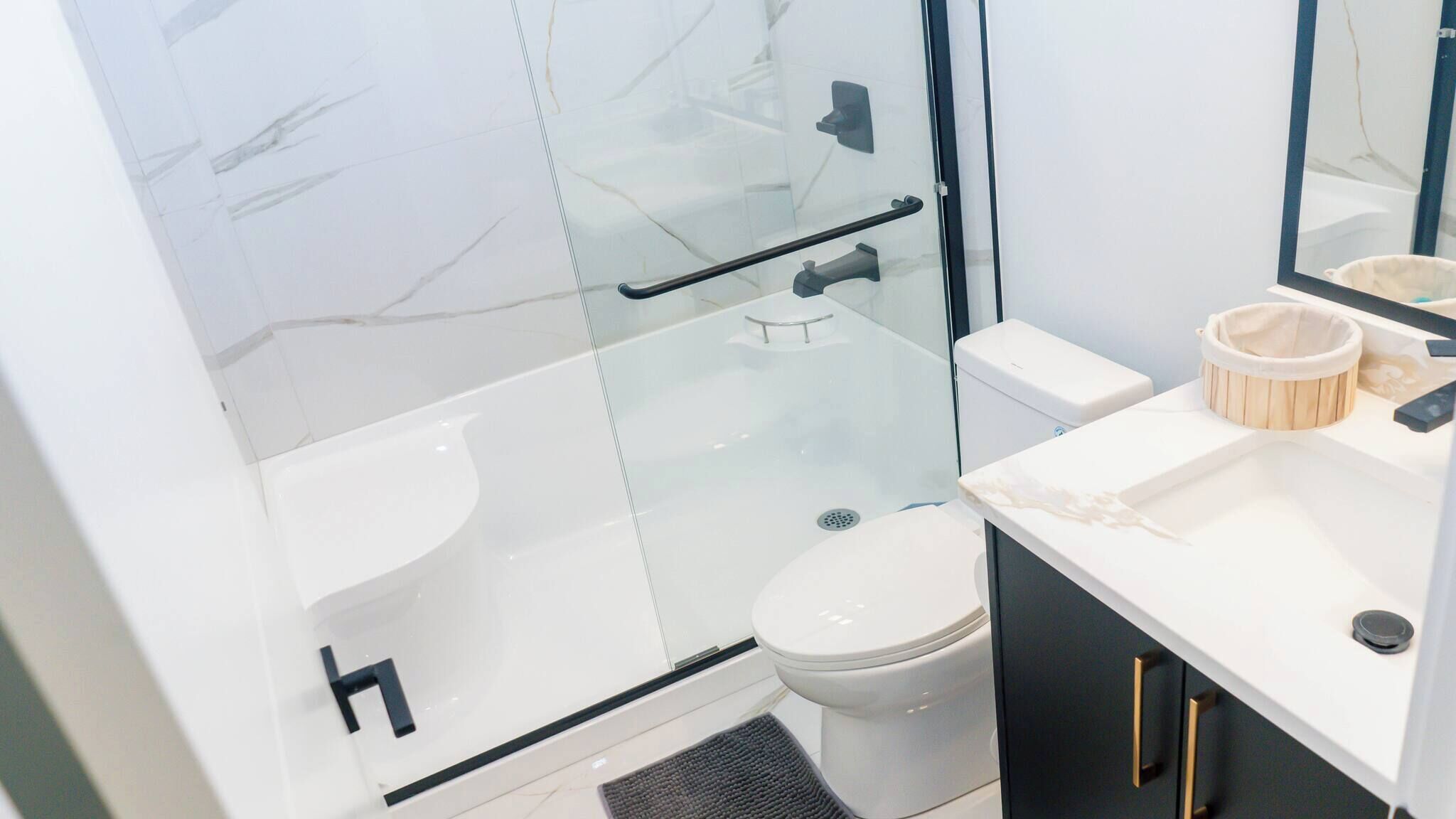 A modern bathroom with a glass shower enclosure, a white toilet, and a vanity with a sink and mirror.
