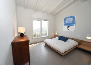 Ein Schlafzimmer mit Bett, Nachttisch, Lampe, Fenster und einem Gemälde.