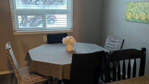 A dining area with a round table, chairs, a vase with flowers, a window with blinds, and artwork on the wall. - 3 bedroom main level home away from Home! Pet friendly with fenced backyard! (Grande Prairie)