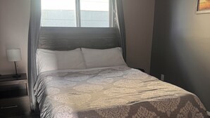 A bedroom with a bed, a nightstand, a lamp, and a window with curtains. - 3 bedroom main level home away from Home! Pet friendly with fenced backyard! (Grande Prairie)