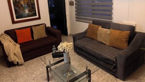 A living room with two sofas, a coffee table, a painting, and a window with blinds.
