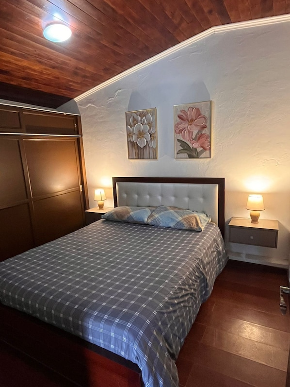 Un dormitorio con cama, mesitas de noche, un armario y dos lámparas de pared.