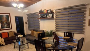 A dining area with a glass table, chairs, a sofa, and a TV.