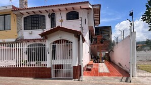 A two-story building with a gated entrance, a tiled patio, and a visible staircase leading to the upper floor.