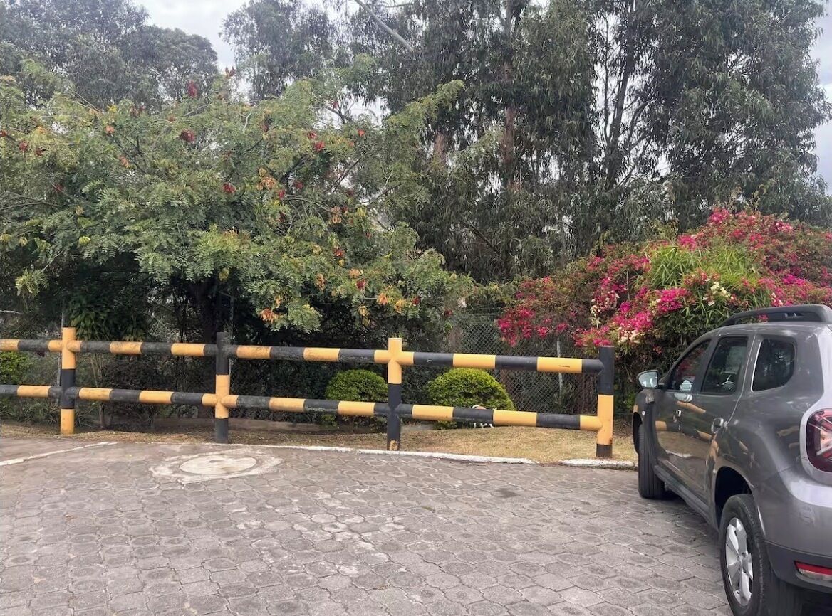 Een omheind parkeergebied met een auto, omringd door bomen en bloeiende planten.
