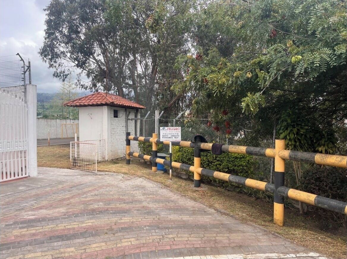 A gated entrance with a sign, a small building with a red-tiled roof, and a brick pathway.