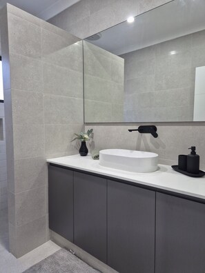 Une salle de bain moderne avec un grand miroir, un lavabo blanc, des meubles sombres et une petite plante.